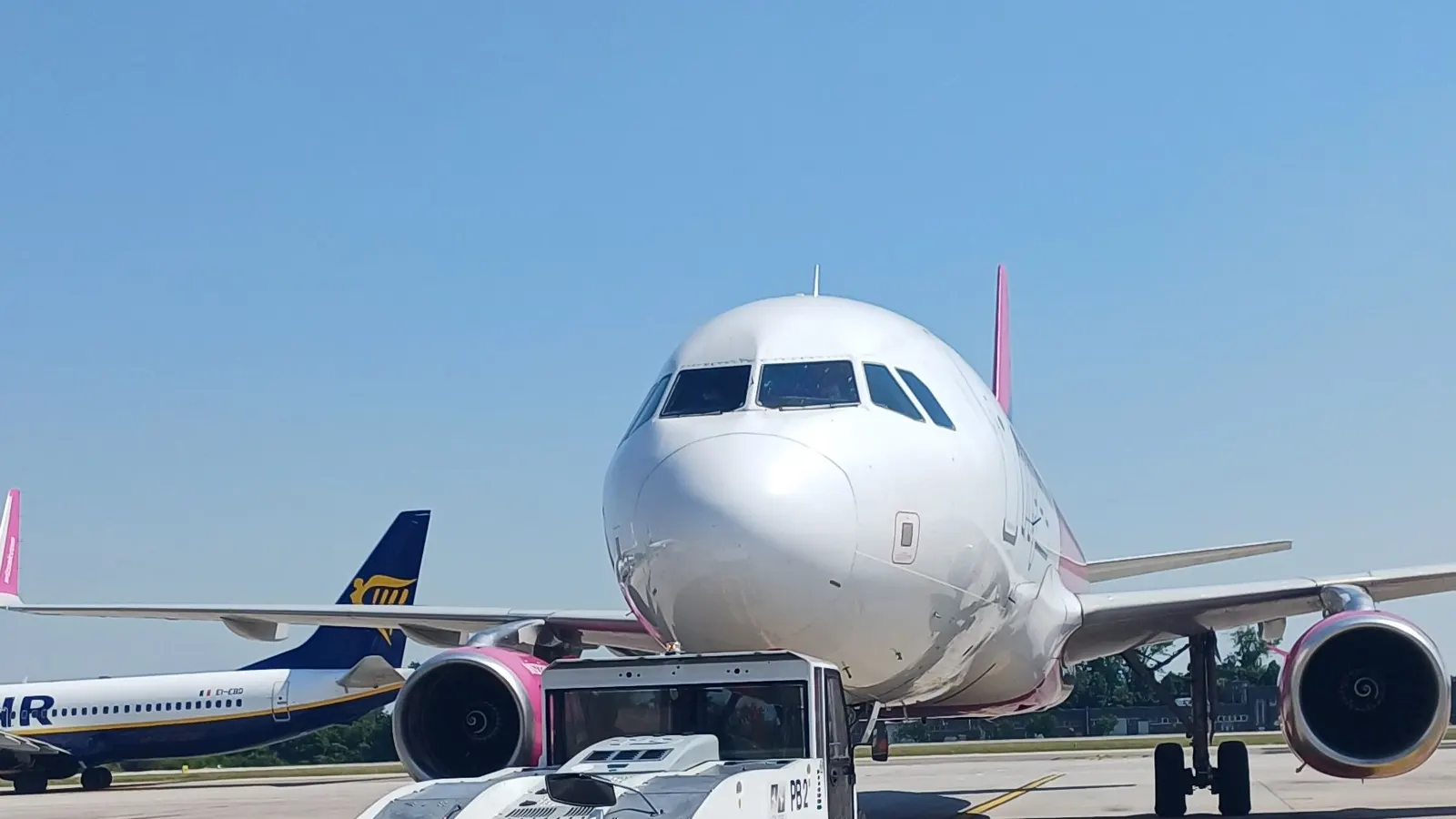 Airbus Wizz Air zepředu na odbavovací ploše, vlevo za ním ocas letadla Ryanair