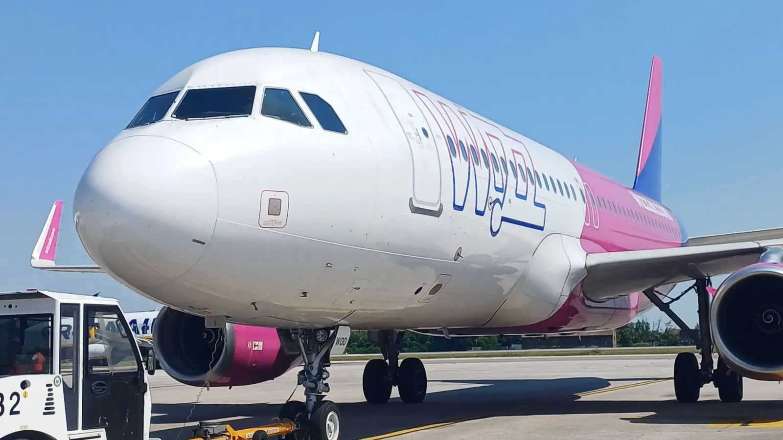 Airbus A320 Wizz Air zepředu na odbavovací ploše, vlevo vlečný traktor